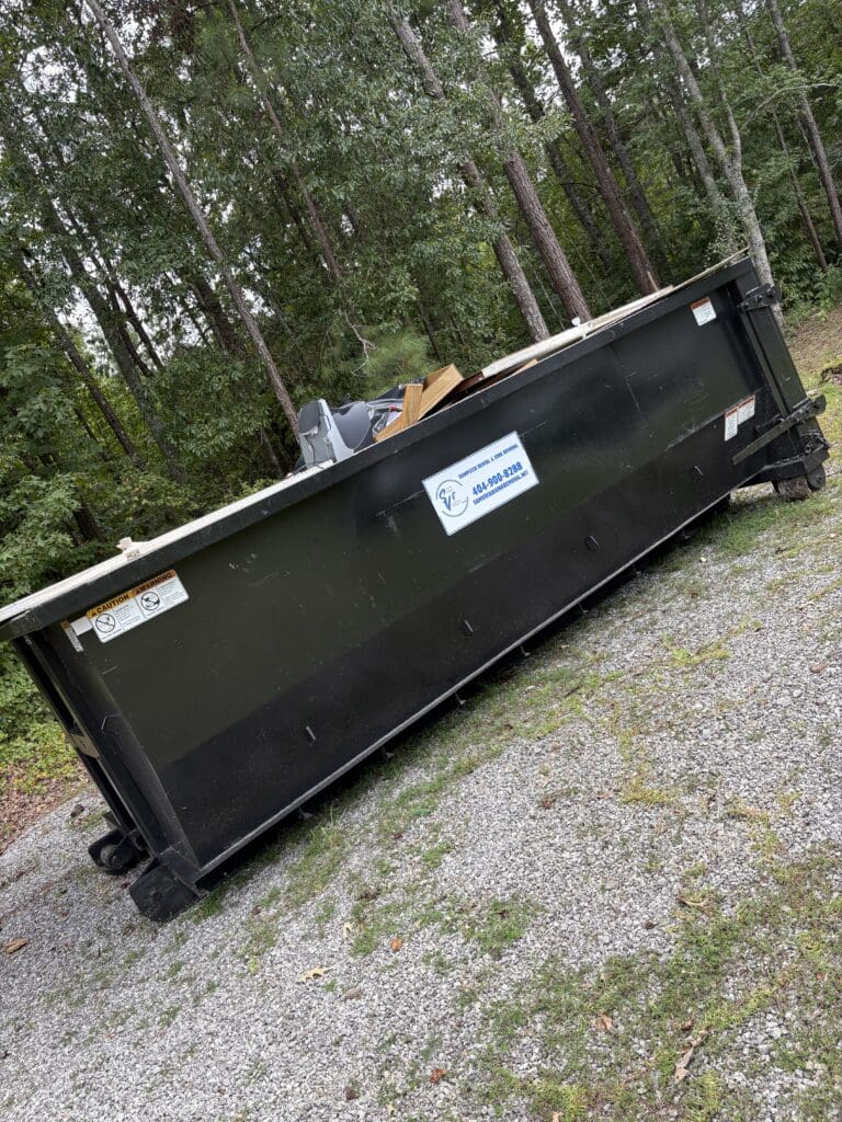 Dumpster on gravel with forest background.